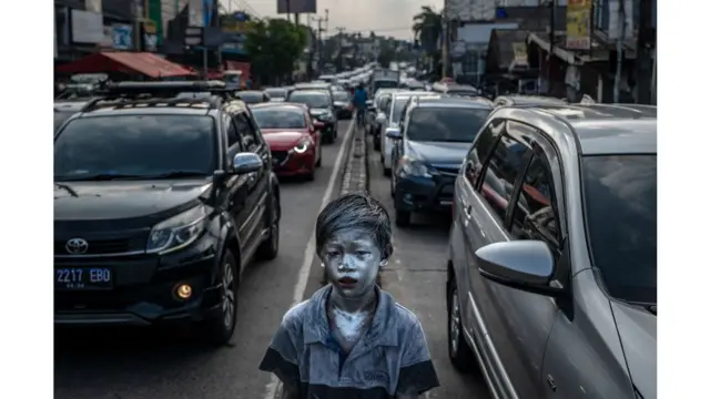 Garoto indonésio com pele pintadaroleta de números de 1 a 20prata anda entre carrosroleta de números de 1 a 20uma rodovia congestionada