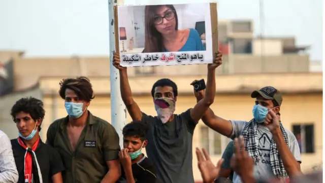 Homem, alguns com máscaras, protestam - um deles mostra cartaz com fotoMia Khalifa