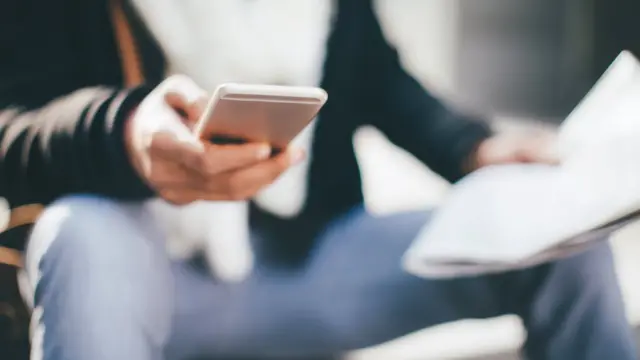Man reading newspaper and texting messages