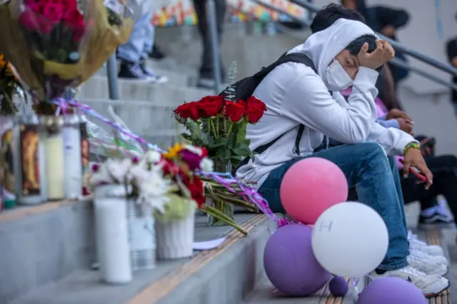 Jovem sentadoesporte da sorte betescadaria observa homenagens para Melanie ali colocadas, como velas e flores