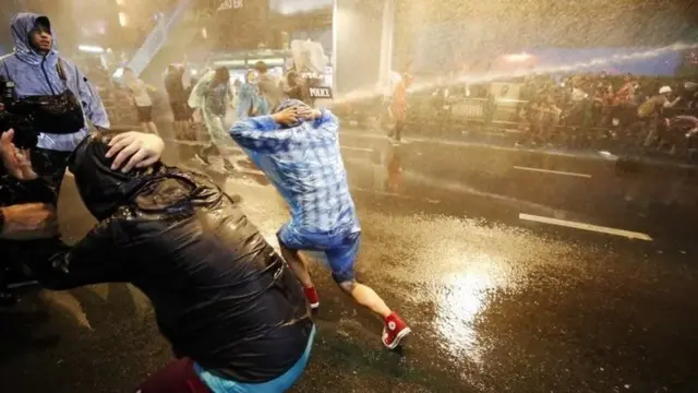 Pro-democracy protesters react as riot police fire water canons during an anti-government protest in Bangkok, Thailand, 16 October 2020