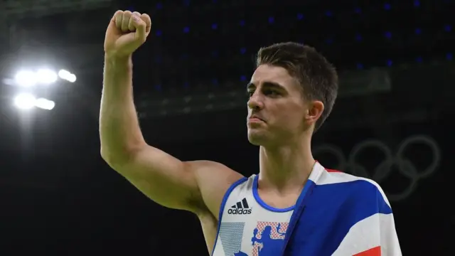Max Whitlock, İngiltere bayrağı üzerinde yumruğu havada başarısını kutluyor.