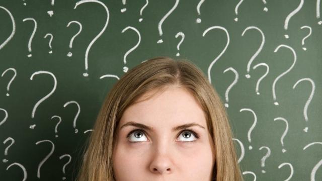 Thinking woman in front of question marks written blackboard