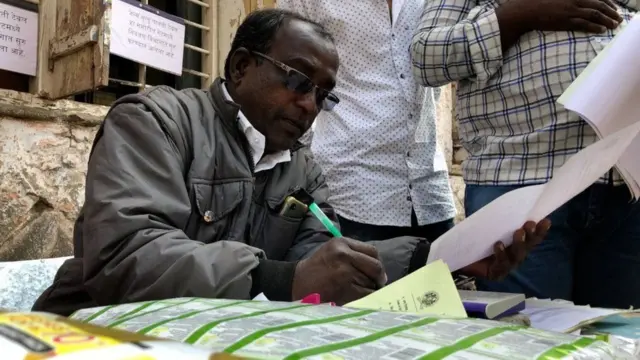 લાંબી લાઈનોમાં વચ્ચે કામ કરતાં અધિકારી