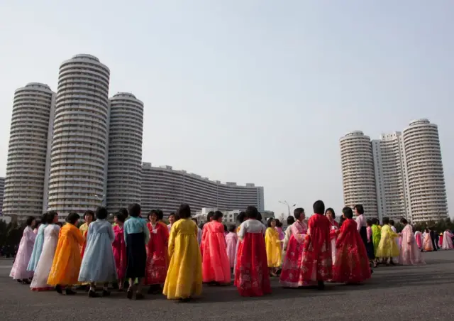 Mujeres vestidas con el traje tradicional frente a unos bloques de apartamentos.