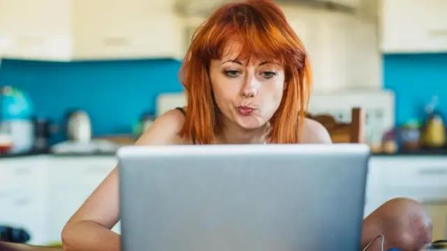 Una joven sentada frente a su laptop con rostro dudoso