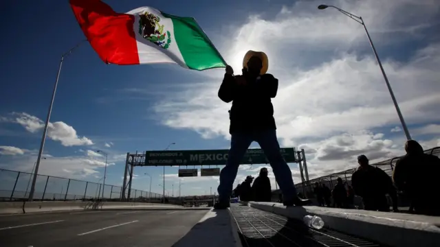 Um homem acena com uma bandeira do México, perto da fronteira dos EUA