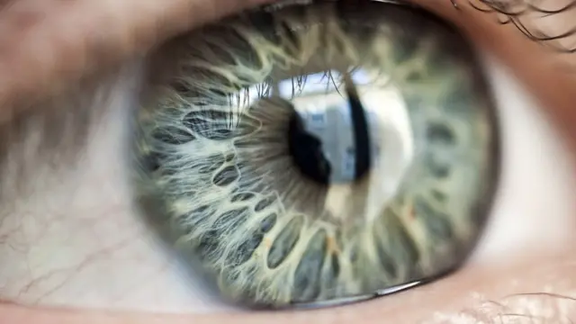 Ojo de cerca en el que se ve la reflexión de una persona frente a una ventana