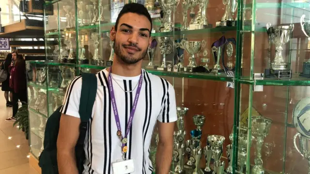 Чоловік у білій з чорним футболці дивиться на камеру.