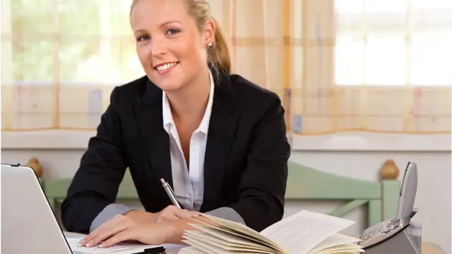 Усміхнена жінка з комп'ютером, записником і телефоном