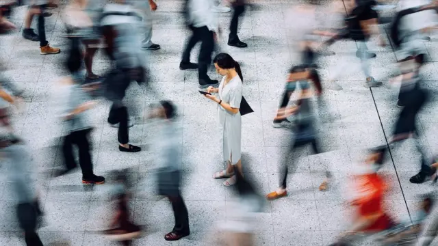 Mulher parada olhando celular enquanto outras pessoas caminham rápido ao redor