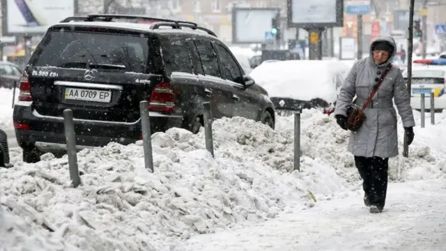 Una mujer camina junto a unos montículos de nieve acumulados al lado de una autopista en Kiev, Ucrania, el nueve de enero de 2017.