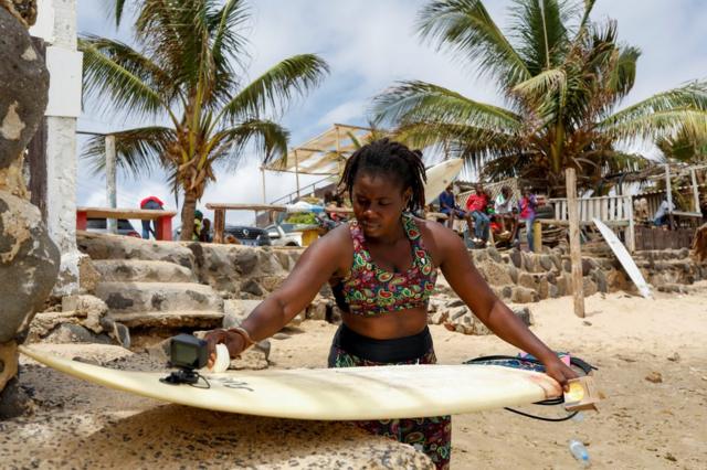 Khadjou Sambe cire sa planche de surf sur la plage