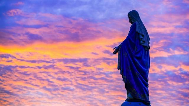 Estátua de Nossa Senhora sob um céu multicolorido pelo por-do-dol