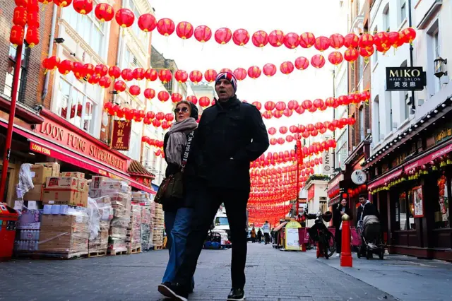 Люди идут по улице, сверху висят китайские бумажные фонари