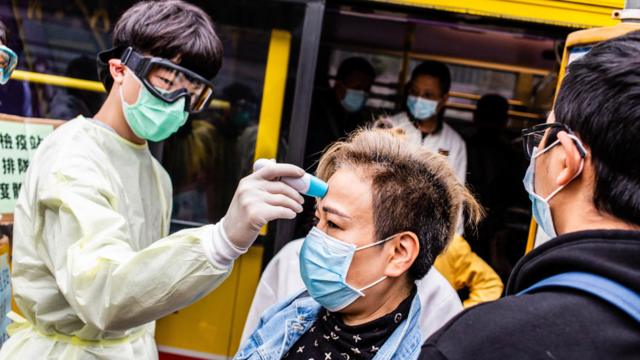 A volunteer measures a passenger's body temperature in Hong Kong