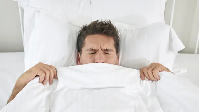 Hombre en la cama tapado en el edredón.