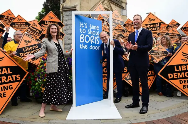 فاز الديموقراطيون الليبراليون في الانتخابات الفرعية في تيفرتون وهونيتون، مما أدى إلى إلغاء أغلبية المحافظين بأكثر من 24,000 صوت. فاز ريتشارد فورد (يمينا) بمقعد ديفون بأكثر من 22,000 صوت بعد أن شهدت الدائرة تأرجحا بنسبة 30 في المئة تقريبا. تم تصويره هنا مع زعيم الحزب إد ديفي، وويندي تشامبرلين.