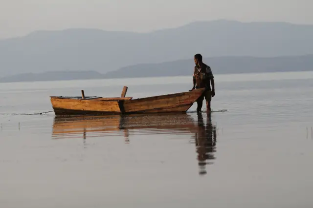 አሳ አስጋሪ በሐይቅ ውስጥ ጀልባውን ተደግፎ