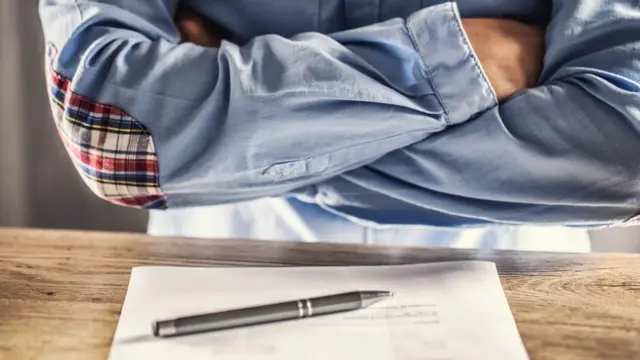 Una persona cruza los brazos ante un contrato.