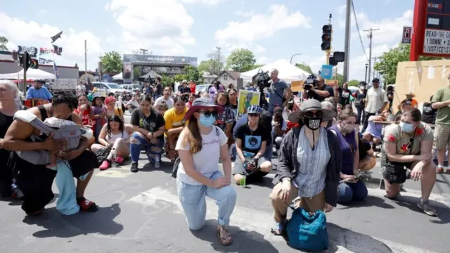 Dezenas de pessoas ajoelhadas em praça durante o dia