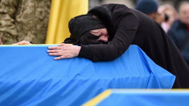 Uma mulher na Ucrânia chora abraçando o caixão de um familiar morto