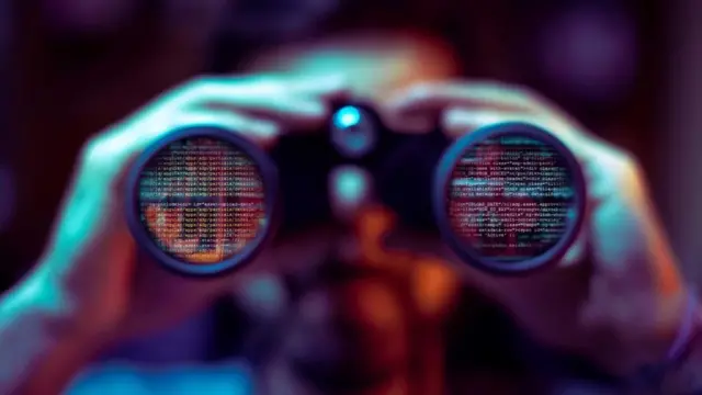 Un hombre mirando por unos binoculares, en cuyas lentes se ven reflejados códigos de computación