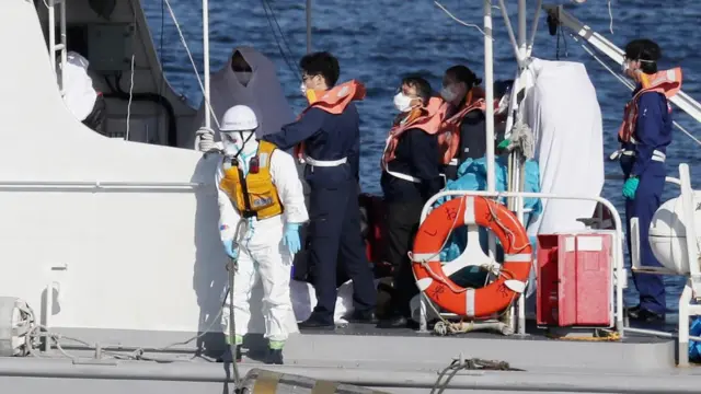 Asistentes médicos transfieren a una persona contagiada (en la foto, envuelta en una sábana blanca) desde el crucero al bote de rescate.