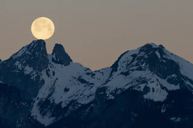 The full moon sets behind the mountains including the twin peaks of Les Jumelles in the Chablais Valaisan, seen from Fenalet-sur-Bex, Switzerland, on 18 January 2022