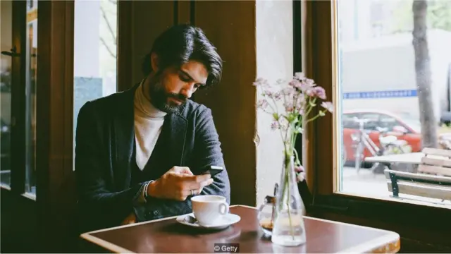 Homem olha celular enquanto toma café