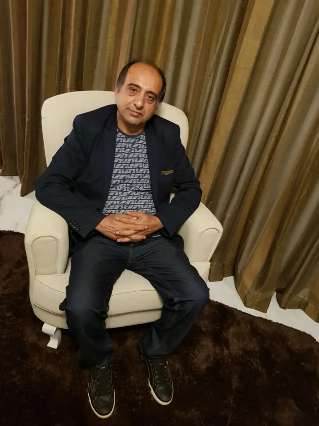 Paknoosh Kharaghani, sentado em poltrona em um quarto de hotel. Ainda adolescente, ele fugiu da guerra Irã-Iraque e de perseguição religiosa no país em 1987. No ano seguinte, se mudou para o Brasil