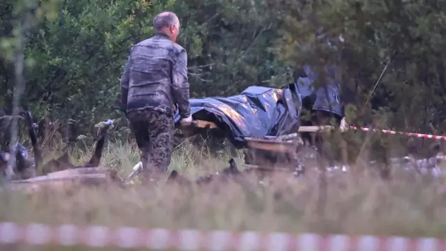 Emergency specialists carry a body bag from the wreckage of a private jet