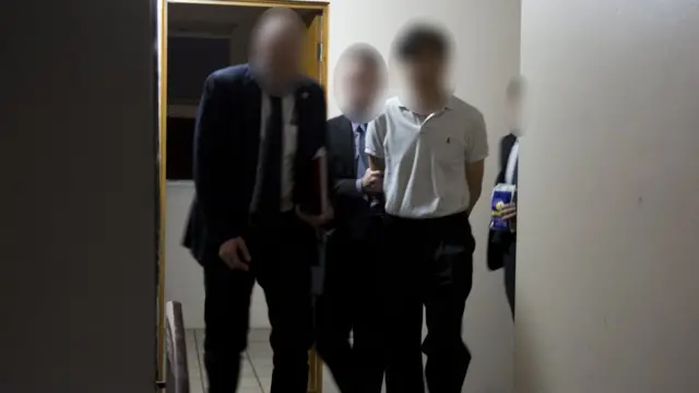 The man is led by police officials inside of a corridor