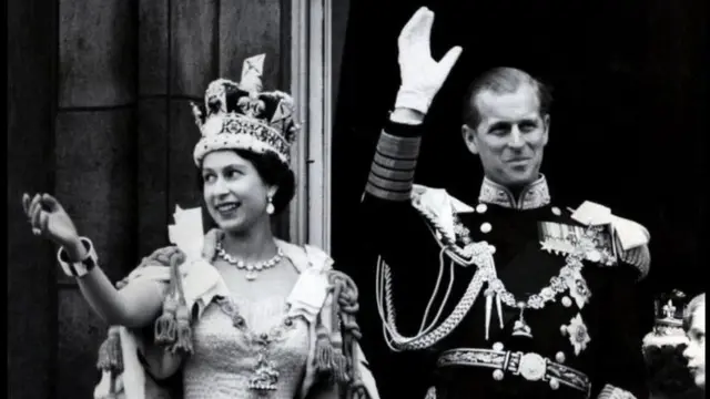 1953: Britains Queen Elizabeth II wears the Imperial State Crown as she and her husband, the Duke of Edinburgh - dressed in the uniform of Admiral of the Fleet - wave from the balcony of Buckingham Palace to the crowds after the Coronation.