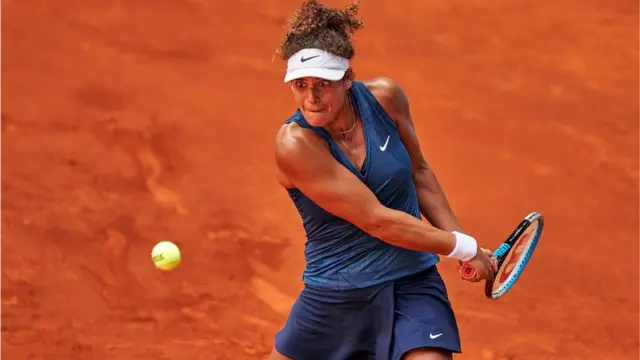 Mayar Sherif playing tennis on clay. The ball is in mid air and she is swinging her racket to hit it. She has a very strained and focused expression.