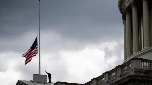 One man lower di flag for di US Capitol in Washington DC