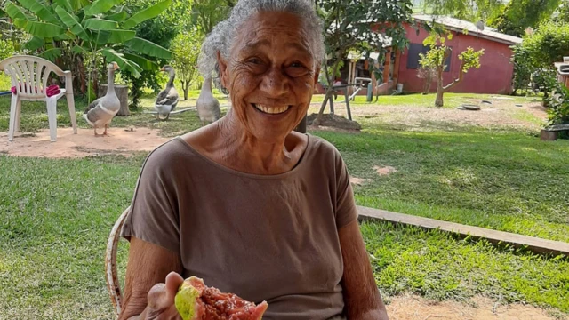 Luzia da Silva sorri para a câmera, goiaba mordida na mão