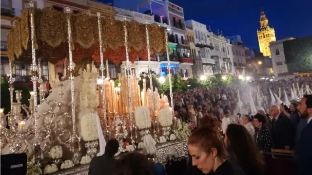 Imagen de la virgen en procesión con La Giralda de fondo