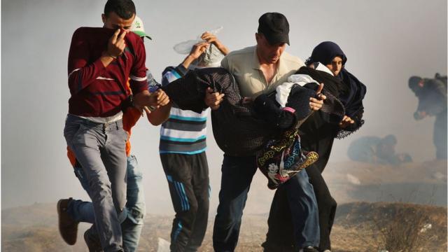 Palestinos atravessam gás lacrimogêneo carregando uma mulher ferida na cerca da fronteira entre a Cidade de Gaza e Israel