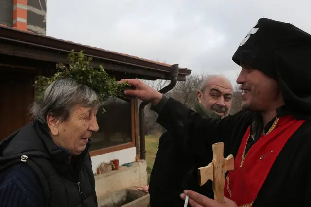 Mladić u ulozi sveštenika blagosilja domaćine “svetom” vodicom kako bi imali zdravlja i sreće tokom godine.