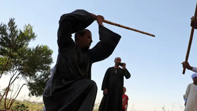 رجل يمسك بالعصا ويستعد لضرب عصا يثبتها شخص آخر