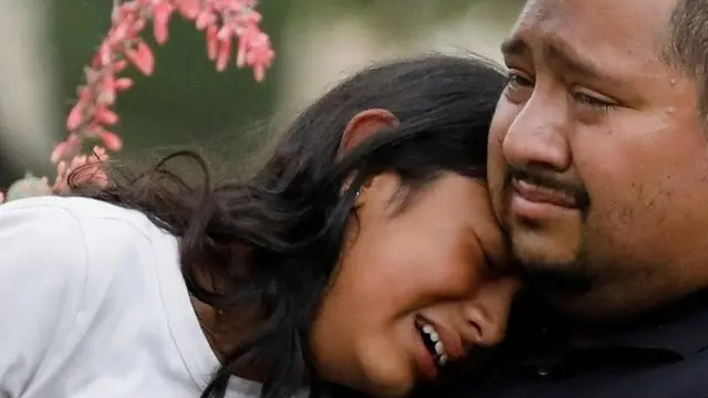 Una muje y un hombre lloran a las puertas de las escuela primaria Robb