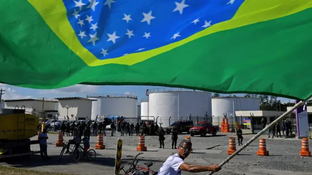 Homem levanta bandeira em frente a refinaria na região metropolitana no Rio