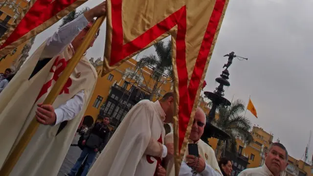 Homens com túnicas com cruzes seguram estandarte