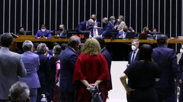Deputados no plenário, olhando em direção à mesa da Câmara, onde todos estão de máscara contra o coronavírus