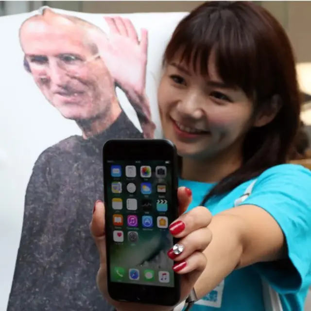 স্মার্টফোনের যুগ: আইফোন হাতে এক তরুণী, পেছনে অ্যাপলের প্রতিষ্ঠাতা স্টিভ জবসের ছবি