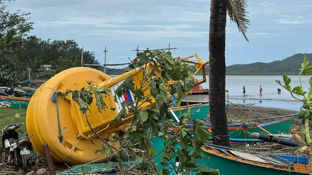 Una boya amarilla en tierra firme tras el paso del tifón junto con ramas y árboles caídos