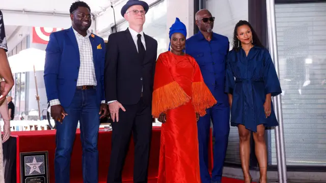 Elle se tient au centre, posant pour la photo. Deux hommes sont à sa droite, et Djimon Hounsou et une femme à sa gauche. Ils se trouvent sur le Walk of Fame.