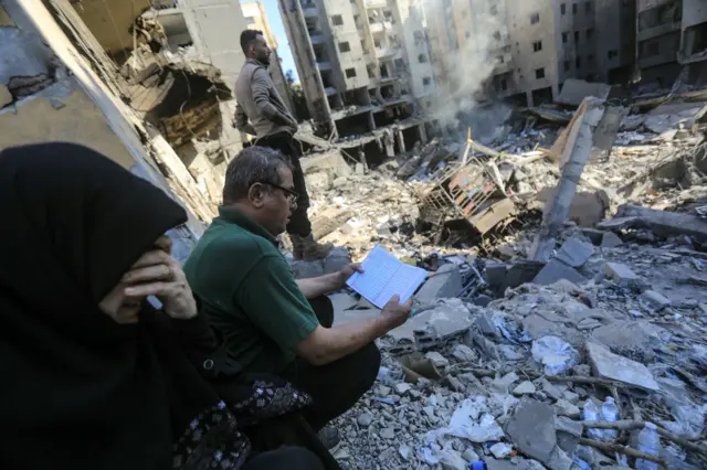 امرأة تبكي فيما يقرأ رجل القرآن أمام أنقاض مبانٍ دمّرها القصف الإسرائيلي في حارة حريك بالضاحية الجنوبية لبيروت بعد اغتيال حسن نصرالله