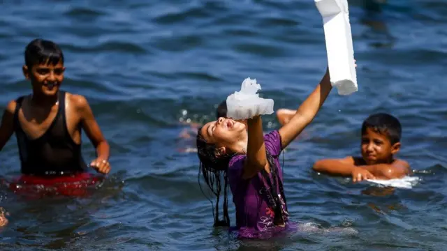 Gazzeli bir kız bir elinde denizanası, diğer elinde kçpükle suda oynuyor